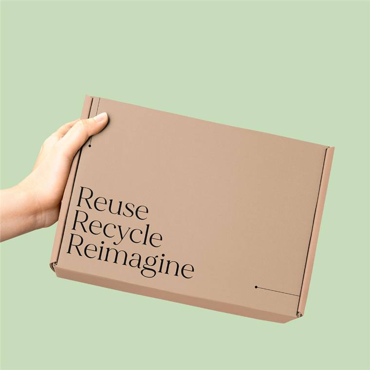 Kraft corrugated mailer box printed with 'Reuse, Recycle, Reimagine' on a sage green backdrop
