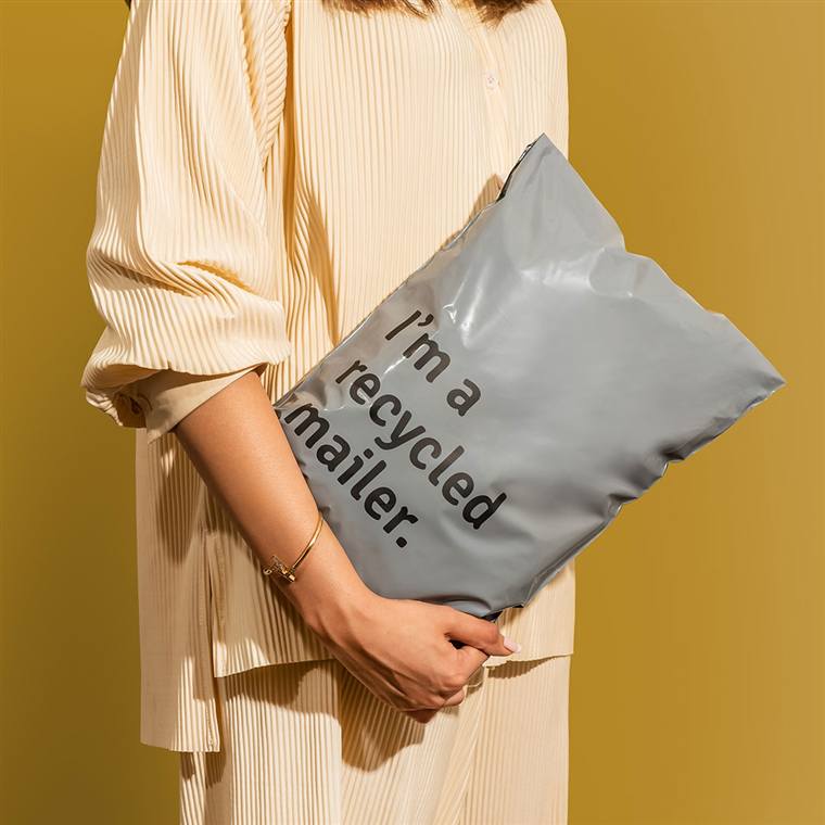Grey recycled poly mailer printed with 'I'm a recycled mailer' held under someone's arm